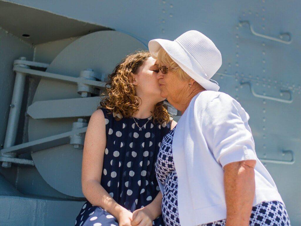 Elderly woman wearing a white hat hugging a young girl with curly red hair