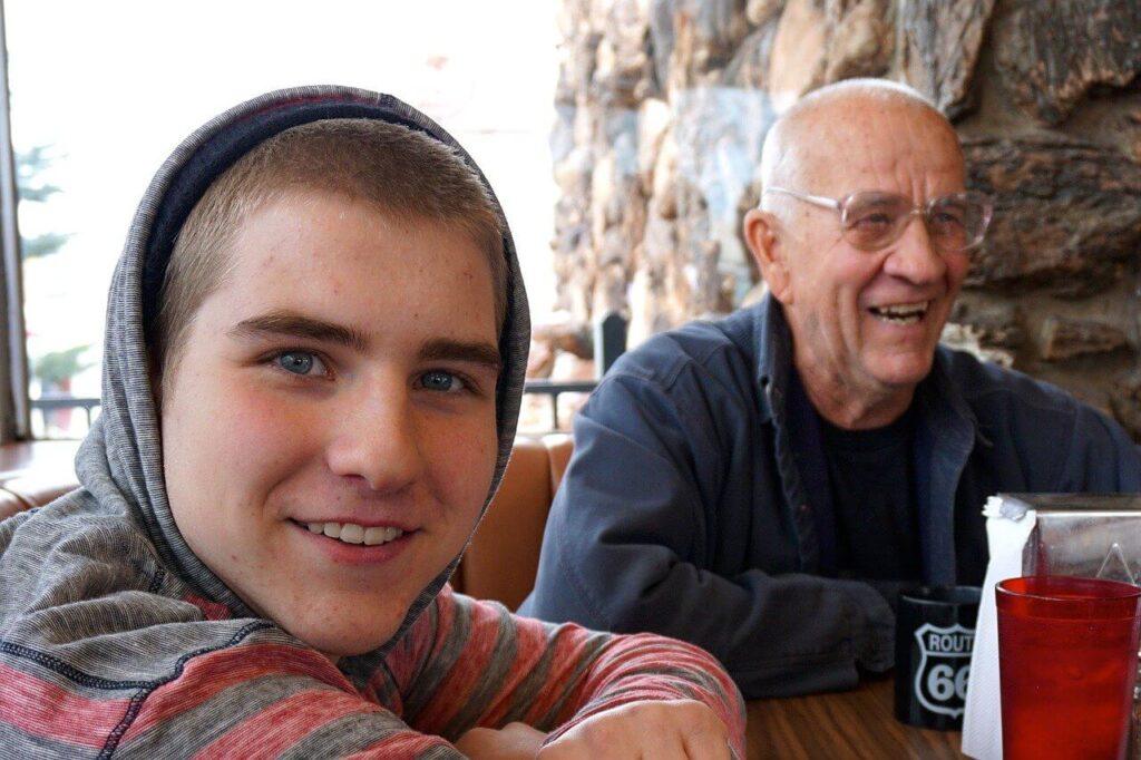 Smiling young man and elderly man sitting together outdoors, enjoying a conversation and quality time.