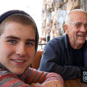 Smiling young man and elderly man sitting together outdoors, enjoying a conversation and quality time.